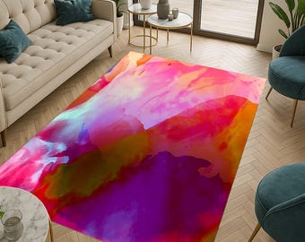 Op de afbeelding: Een groot rechthoekig vloerkleed met een abstract aquarelontwerp. Het vloerkleed heeft een levendige mix van kleuren, waaronder roze, paars, oranje en blauw, waardoor een dynamisch en artistiek patroon ontstaat. Het vloerkleed ligt op een houten vloer.