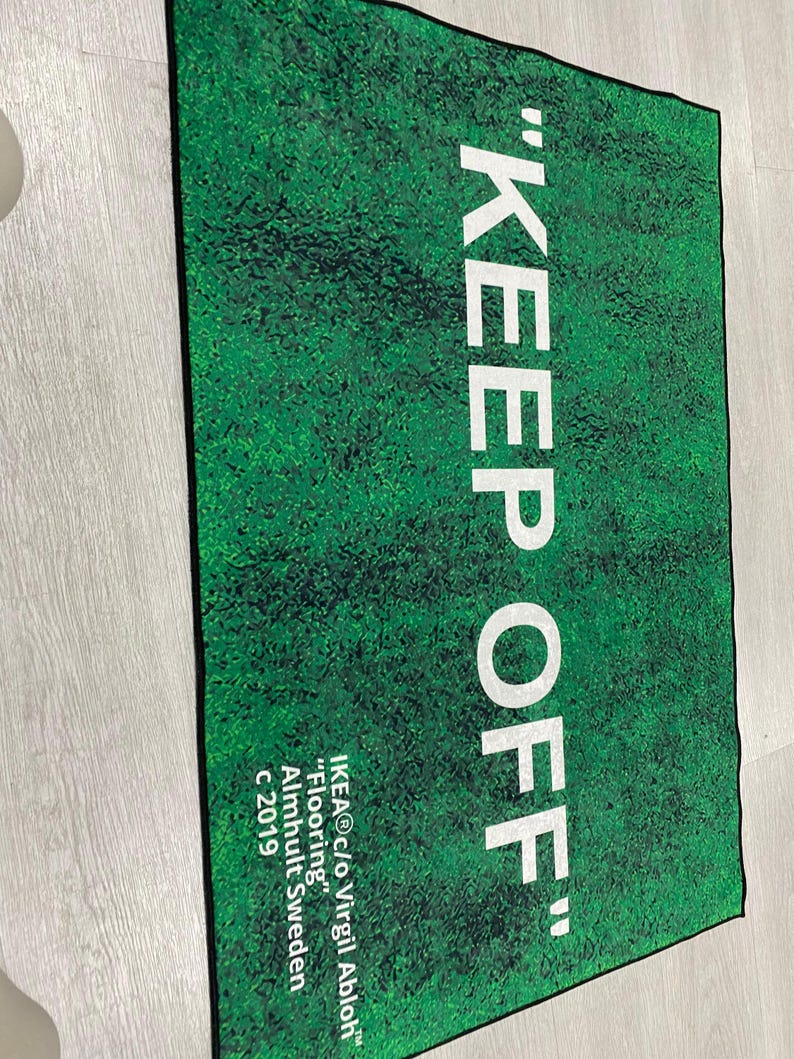 Puede incluir: Una alfombra de bienvenida verde y blanca con el texto "KEEP OFF" en blanco. La alfombra tambi&eacute;n incluye el texto "IKEA&reg;c/o Virgil Abloh&trade;" "Flooring" Almhult Sweden c 2019.