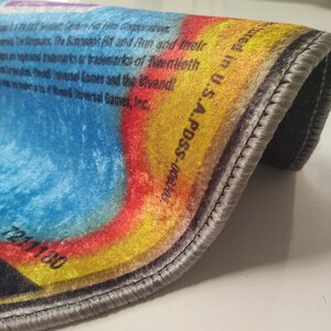 May include: Close-up of a colorful rug with a gray border. The rug has a rainbow design with shades of blue, yellow, red, and orange. The text "wed in U.S.A. PDSS-006205" is printed on the rug. The rug has a number "7211180" printed on the bottom left corner.