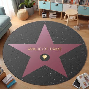 May include: A round, gray and pink rug with a large pink star in the center. The star has the words "Walk of Fame" written in gold lettering and a small gold film camera icon in the center.