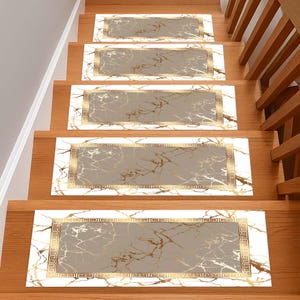 May include: Stair treads with a marble design. Each tread features a gray center with gold veining, framed by a white border and a gold Greek key pattern. The treads are installed on wooden stairs with a wooden handrail.