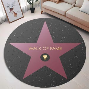 May include: A round, gray and pink rug with a pink star in the center. The star has the words "Walk of Fame" written in gold lettering and a gold film camera icon in the center.