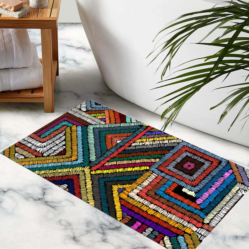 May include: A rectangular bath mat with a vibrant, geometric pattern. The mat displays an embroidered-style design of squares and rectangles in red, orange, yellow, blue, green, and white. The mat is placed on a marble floor.