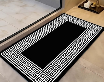 Könnte beinhalten: Eine rechteckige, schwarze Fußmatte mit einem weißen griechischen Schlüsselbordüren-Design. Die Matte liegt vor einer Tür und zeigt eine schlichte, aber elegante Ästhetik. Das Design ist symmetrisch und erzeugt einen sauberen, modernen Look.