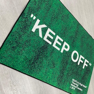 Puede incluir: Una alfombra verde con el texto "KEEP OFF" en letras blancas. La alfombra est&aacute; hecha por IKEA en colaboraci&oacute;n con Virgil Abloh.