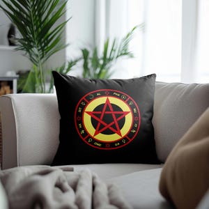 Può includere: Cuscino nero con un pentagramma rosso all'interno di un cerchio giallo con testo nero attorno al cerchio. Il testo recita "AL PHA NU IT GA OME DT HA ZL", con simboli tra ogni parola.