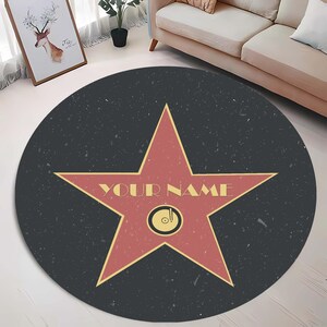 May include: A round black and red rug with a large red star in the center. The star has a yellow outline and the words "YOUR NAME" written in yellow letters. The rug has a speckled texture.