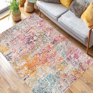 May include: A rectangular area rug with a distressed, abstract design. The rug features a blend of colors, including orange, pink, blue, and purple, with a cream-colored background. The rug is placed on a hardwood floor.