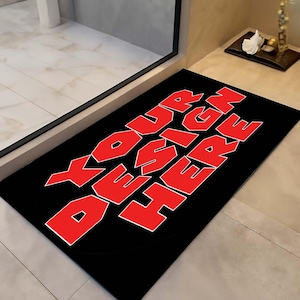 May include: Black rectangular doormat featuring the text "YOUR DESIGN HERE" in bold red letters with a white outline. The mat is positioned in front of a glass door.