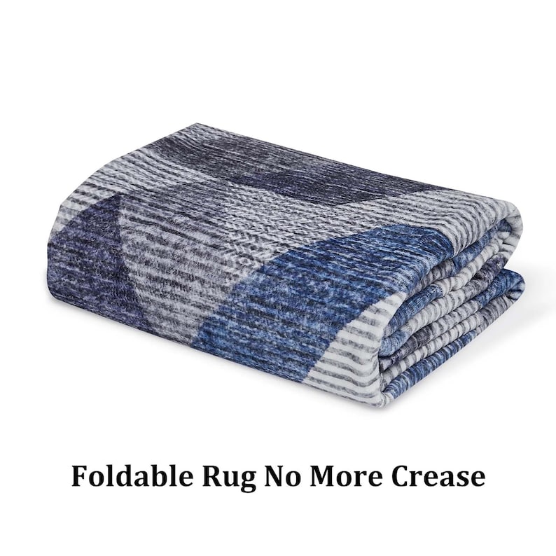 K&ouml;nnte beinhalten: Ein gefalteter blauer und wei&szlig;er Teppich mit geometrischem Muster. Der Teppich besteht aus einem weichen, pl&uuml;schigen Material und ist so konzipiert, dass er faltbar ist, was ihn einfach zu verstauen und zu transportieren macht. Der Text "Foldable Rug No More Crease" ist auf dem Bild sichtbar.