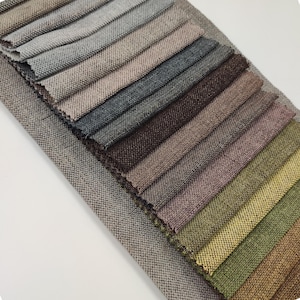 May include: A collection of fabric swatches in various shades of brown, gray, green, and beige. The swatches are arranged in a fan shape, with the lightest colors at the top and the darkest colors at the bottom.