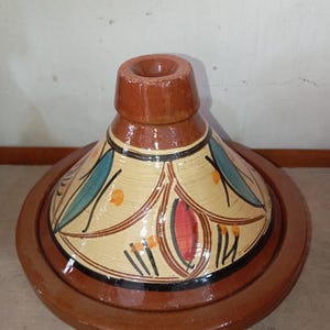 Peut inclure: Un tajine en céramique marron avec un couvercle conique et une large base. Le couvercle est décoré d'un fond beige et de motifs floraux colorés en bleu, rouge et orange. Le pot est conçu pour la cuisine et le service de plats marocains.