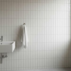 Könnte beinhalten: Eine moderne Badezimmerszene mit einem weißen rechteckigen Waschbecken mit Chromarmaturen, einem weißen Handtuch, das an einem Metallhaken hängt, und weißen vertikal gefliesten Wänden. Der Boden ist hellgrau.