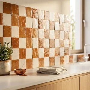 May include: A kitchen with a white countertop and light wood cabinets. The backsplash features a checkerboard pattern of brown and white tiles. A small potted plant and a copper bowl are on the counter.
