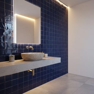 Puede incluir: Diseño de baño moderno con una pared de azulejos azul marino y un tocador flotante de hormigón. El tocador sostiene un lavabo de piedra y una pequeña planta suculenta. Un gran espejo con iluminación integrada cuelga sobre el lavabo.