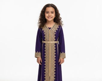 Può includere: Una bambina indossa un lungo abito viola con ricami dorati. L'abito ha maniche lunghe e una cintura dorata abbinata. I ricami dettagliati adornano la parte anteriore e le maniche.