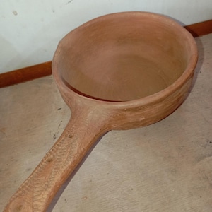 Peut inclure: Une louche en terre cuite faite à la main, avec un large bol et un long manche texturé. La louche est de couleur marron chaud et terreux, et la poignée présente des détails sculptés. Le bol mesure environ 15 cm de diamètre.