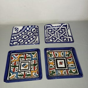 Peut inclure: Quatre plats carrés en céramique avec une bordure bleue. Deux plats présentent des motifs géométriques blancs et bleus. Les deux autres ont des motifs floraux colorés avec des accents rouges, verts, jaunes et bleus. Ces plats décoratifs sont parfaits pour servir des collations.