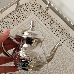 Peut inclure: Une théière en argent avec un motif orné, posée sur un plateau en argent avec un motif décoratif.