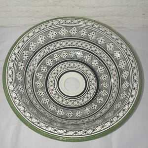 Peut inclure: Un évier en céramique blanche avec un bord vert et des motifs géométriques noirs et blancs complexes.
