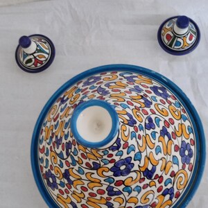 Peut inclure: Une tagine en céramique bleue et blanche avec un motif floral coloré. La tagine a un couvercle rond avec un bouton sur le dessus. La tagine est un pot de cuisson marocain traditionnel.