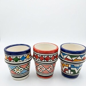 Peut inclure: Trois tasses en céramique ornées de motifs géométriques peints à la main dans des couleurs vives comme le rouge, le bleu, le vert et le jaune. Chaque tasse présente un intérieur blanc, un bord évasé et des lignes noires complexes.