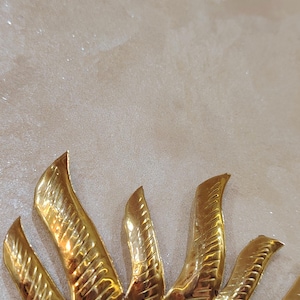 K&ouml;nnte beinhalten: Ein goldfarbener Sonnenspiegel aus Metall mit einem dekorativen Design. Der Spiegel ist rund und hat einen erh&ouml;hten Rand.