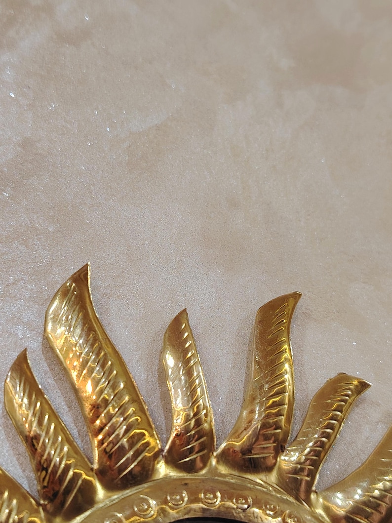 K&ouml;nnte beinhalten: Ein goldfarbener Sonnenspiegel aus Metall mit einem dekorativen Design. Der Spiegel ist rund und hat einen erh&ouml;hten Rand.