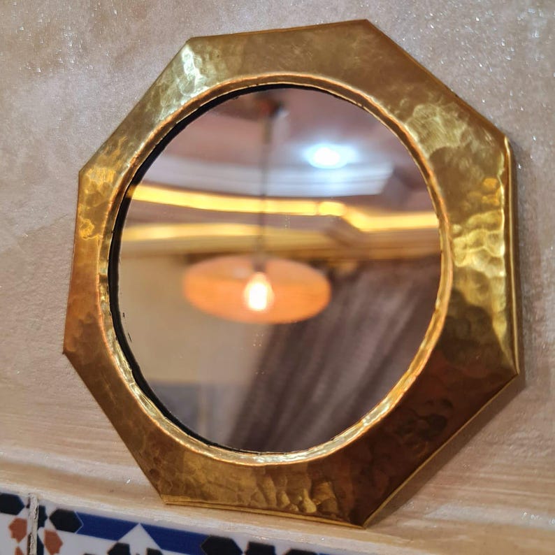 May include: A gold octagonal mirror with a hammered finish. The mirror has a round reflective surface.