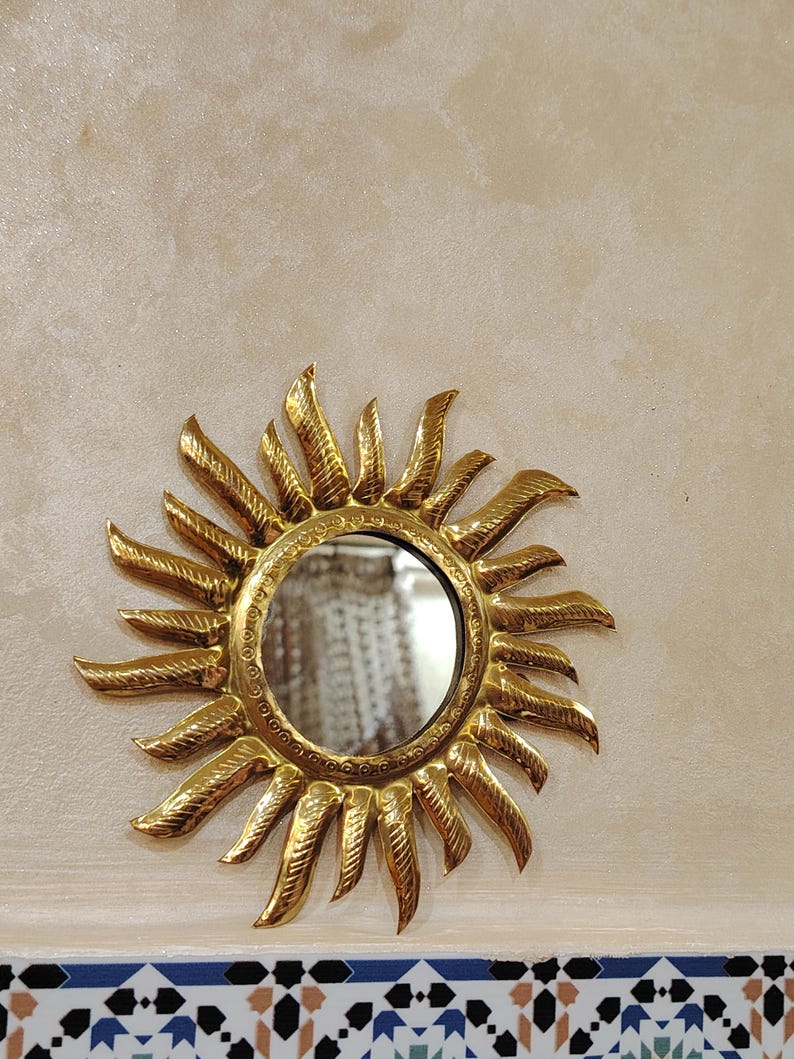 K&ouml;nnte beinhalten: Ein goldener Sonnenspiegel mit einem runden Spiegel in der Mitte. Der Spiegel ist von einem dekorativen Sonnenstrahlendesign umgeben.