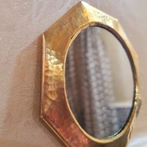 May include: A gold octagonal mirror with a hammered finish. The mirror has a round reflective surface.