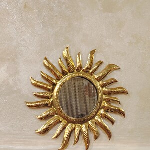 K&ouml;nnte beinhalten: Ein goldener Sonnenspiegel mit einem ovalen Spiegel in der Mitte. Der Spiegel ist von einem dekorativen Sonnenstrahlenmuster umgeben.