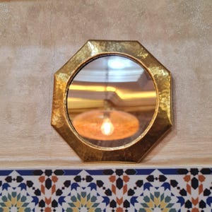 May include: A gold octagonal mirror with a hammered finish. The mirror reflects a light fixture with a light bulb.