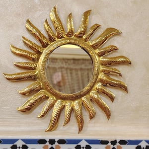 K&ouml;nnte beinhalten: Ein goldener Sonnenspiegel mit einem runden Spiegel in der Mitte. Der Spiegel ist von einem dekorativen Sonnenstrahlenmuster umgeben.