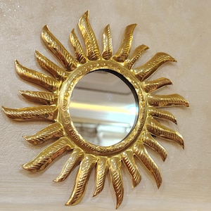 K&ouml;nnte beinhalten: Ein goldener Sonnenspiegel mit einem runden Spiegel in der Mitte. Der Spiegel ist von einem dekorativen Sonnenstrahlenmuster umgeben.