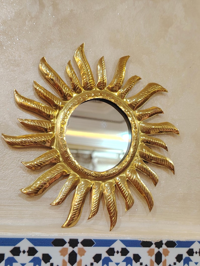 K&ouml;nnte beinhalten: Ein goldener Sonnenspiegel mit einem runden Spiegel in der Mitte. Der Spiegel ist von einem dekorativen Sonnenstrahlenmuster umgeben.