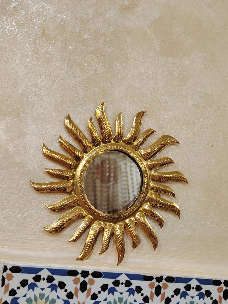 K&ouml;nnte beinhalten: Ein goldener Sonnenspiegel mit einem runden Spiegel in der Mitte. Der Spiegel ist von einem dekorativen Sonnenstrahlenmuster umgeben.