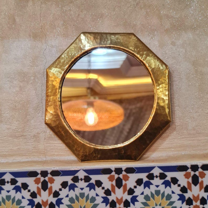 May include: A gold octagonal mirror with a hammered finish. The mirror reflects a light fixture with a round, orange shade.