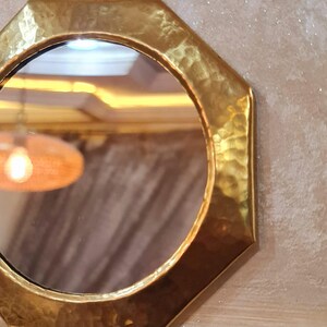May include: Octagonal brass mirror with a hammered finish. The mirror has a round reflective surface.