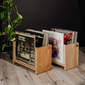 Può includere: Due supporti in legno di colore chiaro per dischi in vinile contenenti diversi album musicali. I dischi in primo piano mostrano le copertine di Tumbleweed Connection di Elton John e Dancing With Strangers di Chris Rea in espositori aperti.
