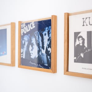 Könnte beinhalten: Drei quadratische Schallplattenrahmen aus hellem Holz, die jeweils ein anderes Plattencover enthalten. Der mittlere Rahmen zeigt das Album Reggatta de Blanc von The Police mit einem bläulichen Foto von drei Bandmitgliedern.