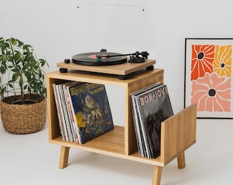May include: A light oak wood record player stand with four angled legs, featuring a top surface for a turntable and two lower compartments for vinyl records. The stand holds multiple records, including albums by Iron Maiden and Bon Jovi.