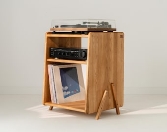 May include: A light brown wooden media console with a top surface holding a black turntable with a clear cover, a middle shelf containing a black audio receiver, and a bottom shelf storing a collection of vinyl records in their sleeves.