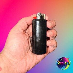 May include: A black lighter with a red ignition button. The lighter is held in a hand against a colorful background. The lighter has a metallic top.