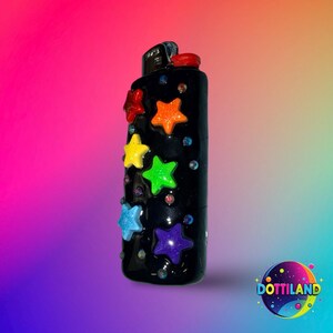 May include: Black lighter decorated with colorful star-shaped embellishments. The stars are in red, orange, yellow, green, blue, and purple. Small, iridescent rhinestones are scattered around the stars. The lighter has a red ignition button.