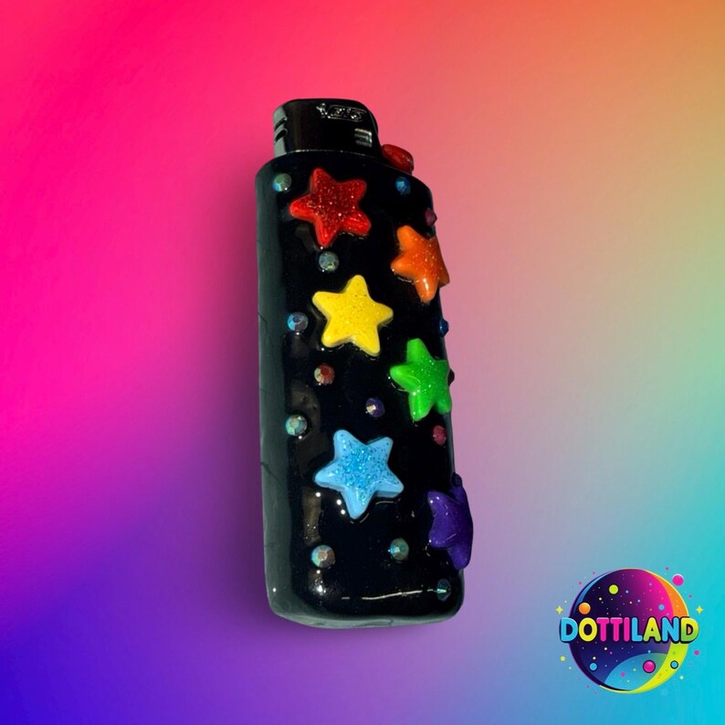 May include: A black lighter decorated with colorful star-shaped embellishments. The stars are in red, orange, yellow, green, blue, and purple. Small, iridescent gems are scattered around the stars. The lighter has a glossy finish.