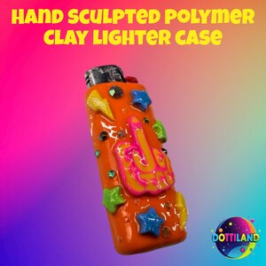 May include: Hand-sculpted polymer clay lighter case in orange, adorned with colorful stars, gems, and a hand gesture. The text "HAND SCULPTED POLYMER CLAY LIGHTER CASE" is displayed in yellow. The lighter case is a unique accessory.