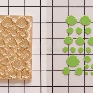 May include: A gold metal mould with a grid of 36 raised, scalloped circles. Next to it is a sheet of green, scalloped circles in various sizes.