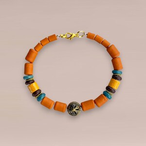 May include: A handcrafted bracelet featuring orange cylindrical beads, interspersed with turquoise, yellow, and brown beads. A gold-colored clasp secures the bracelet. A decorative black and gold bead is centered.