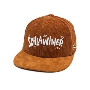 Könnte beinhalten: Eine braune Baseballkappe aus Cord mit einem Besatz aus Wildleder. Die Kappe hat eine weiße Stickerei mit der Aufschrift "SCHLAWINER" auf der Vorderseite.